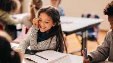 iStock - Elementary Girl Laughing in class girl laughs happily in a primary school class, she is sitting at a table with her her classmates.