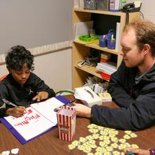 Male Educational Assistant sits with male elementary student playing education game at a table