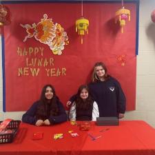 3 Middle school students sitting at a table waiting to hand out coins.