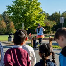 Male wearing a tutu speaks to students outside with a microphone to get them excited for the arrival of Tour de Valley riders.