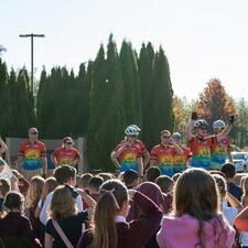 School assembly outside with students looking towards the front where the Tour de Valley group of riders stand waving.