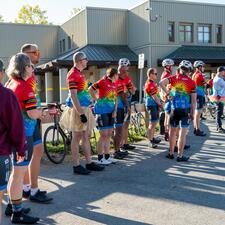 Tour de Valley Riders standing, being introduced by a male who is holding a microphone.