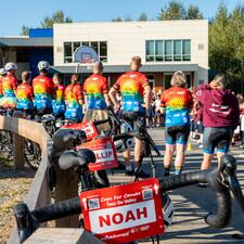 Riders standing in front of students outside with bikes resting against a wooden fence.